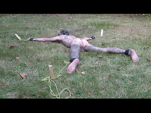 Bound and gagged spreadeagle outdoors biting grass