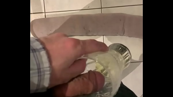 Man pisses in a glass. Cat watches briefly.