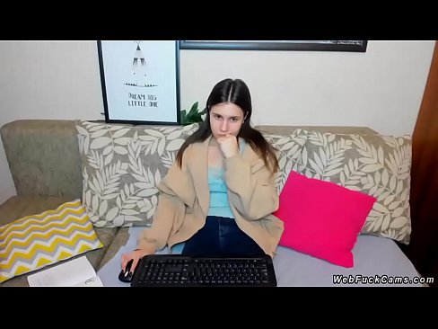 Brunette amateur teen sitting in clothes on the couch and typing on her keyboard while getting remote controlled vibrations from users of webcam show